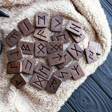 Wooden runes arranged on a textured surface with a candle in the background